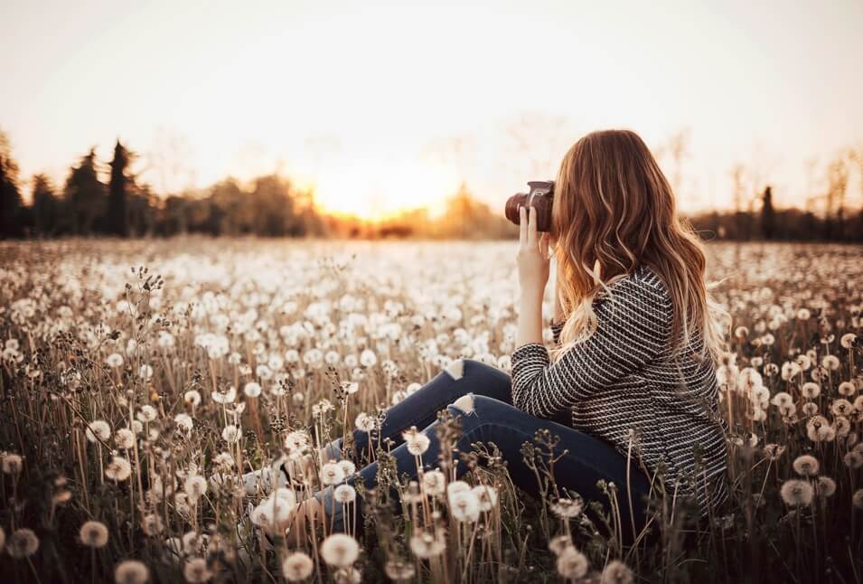 A woman peeping through a camera sitting on a flower field